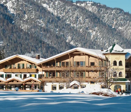 Snow-covered old wooden house in front of forested mountain in winter