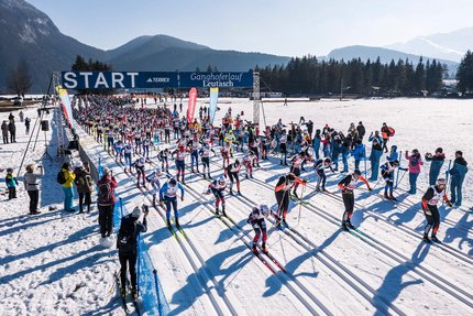 Start eines Langlaufrennens mit vielen Skifahrern auf einer verschneiten Strecke