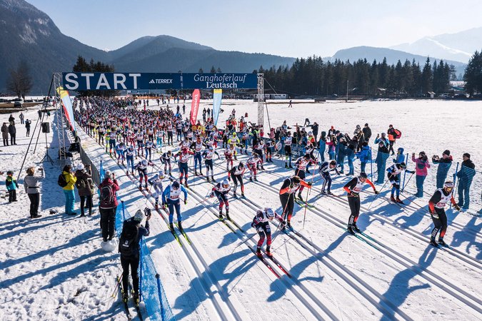 Start eines Langlaufrennens mit vielen Skifahrern auf einer verschneiten Strecke