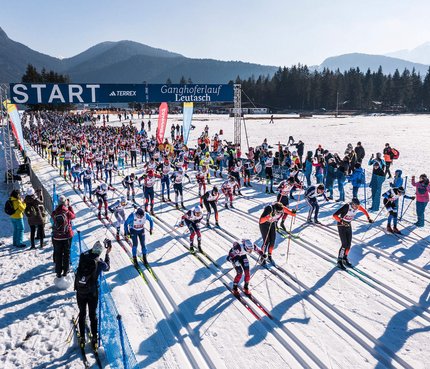 Start eines Langlaufrennens mit vielen Skifahrern auf einer verschneiten Strecke