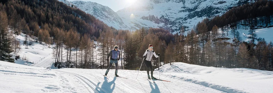 Two people cross-country skiing on snowy mountain landscape in sunshine