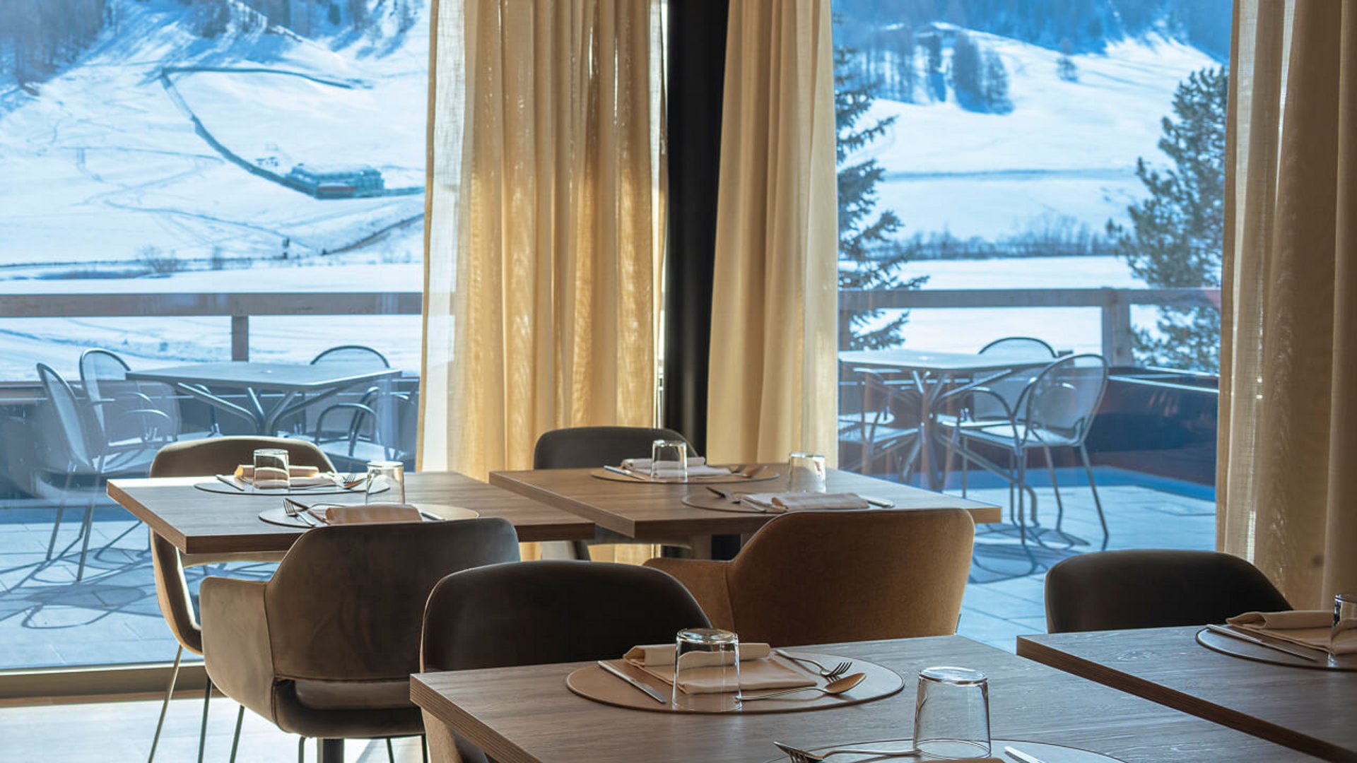 Restaurant mit gedeckten Tischen und Ausblick auf verschneite Berge