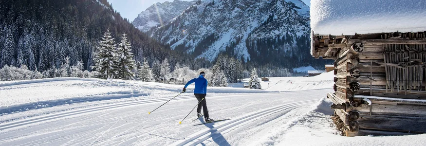 Kleinwalsertal © Dominik Berchtold Langläufer in verschneiter Alpenlandschaft neben einer tief verschneiten Holzhütte