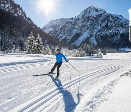 Cross-country skier on a snowy trail surrounded by snow-covered mountains