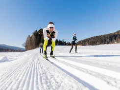 Three people cross-country skiing on groomed snow track under clear blue sky