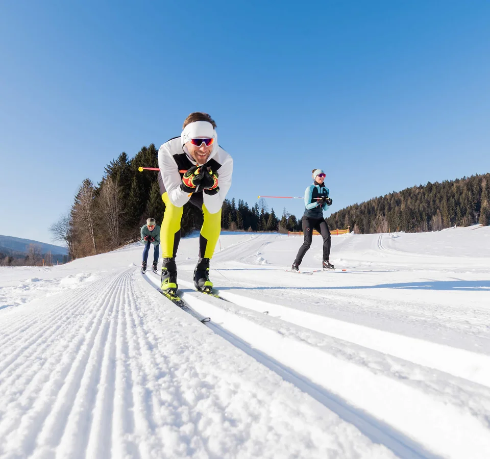 Lungauer Langlauftage © Salzburger Lungau Drei Personen beim Langlaufen auf präparierter Schneestrecke bei Sonnenschein