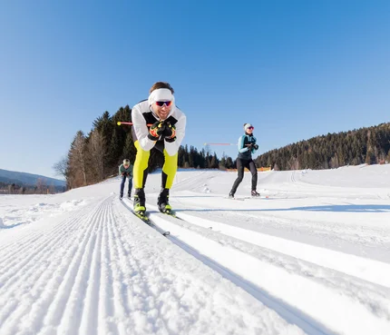 Drei Personen beim Langlaufen auf präparierter Schneestrecke bei Sonnenschein
