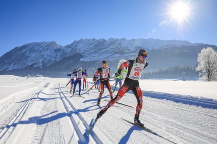 Cross-country skiers racing on snowy mountain trail in bright sunshine