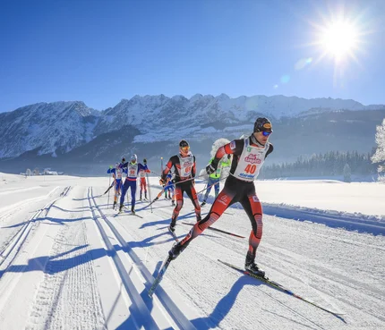 Cross-country skiers racing on snowy mountain trail in bright sunshine