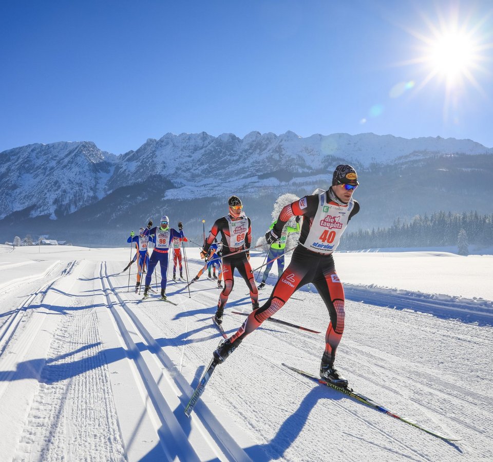 Cross-country skiers racing on snowy mountain trail in bright sunshine