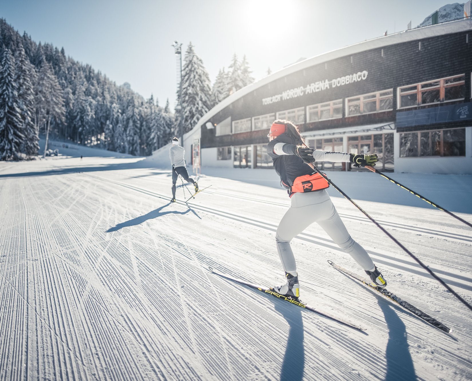 Hobby Biathlon © Kottersteger Langläufer beim Skilanglauf vor verschneiter Waldlandschaft und Gebäude