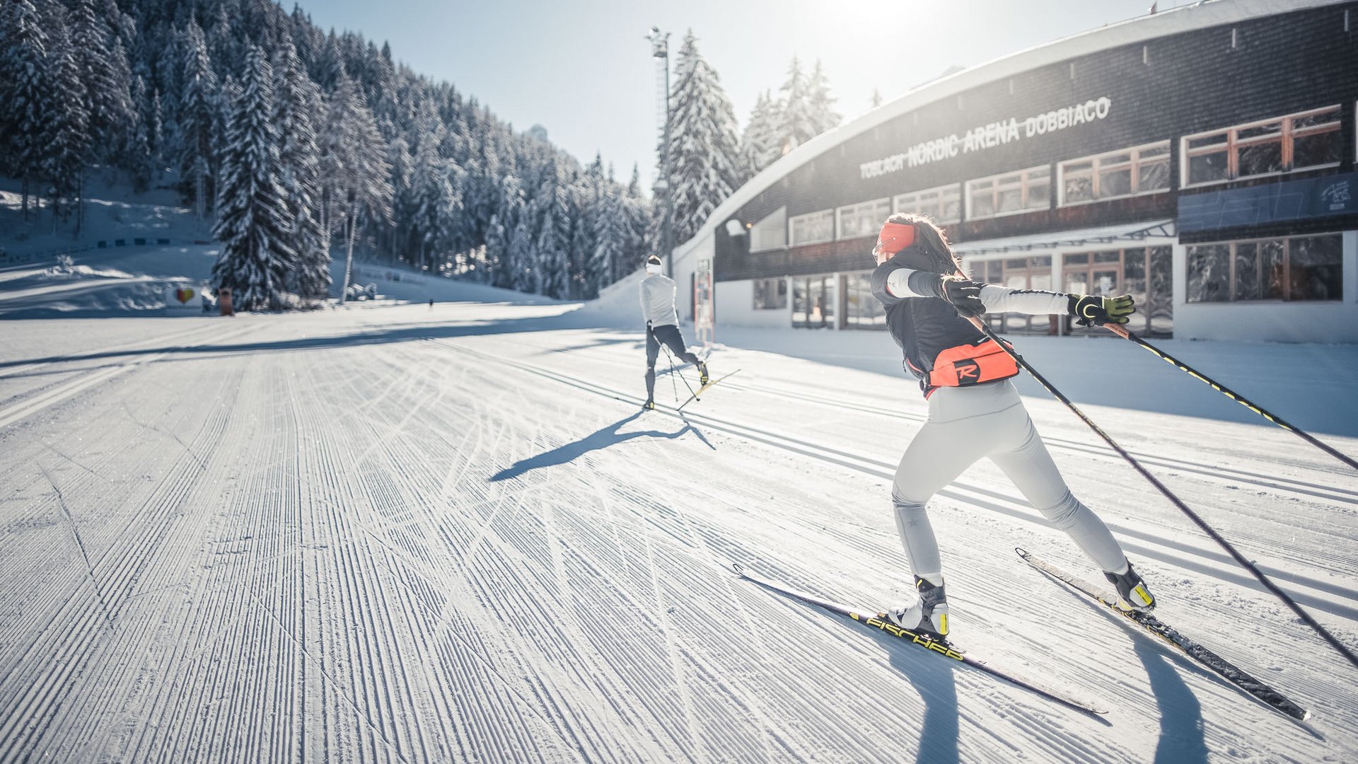 Langläufer beim Skilanglauf vor verschneiter Waldlandschaft und Gebäude