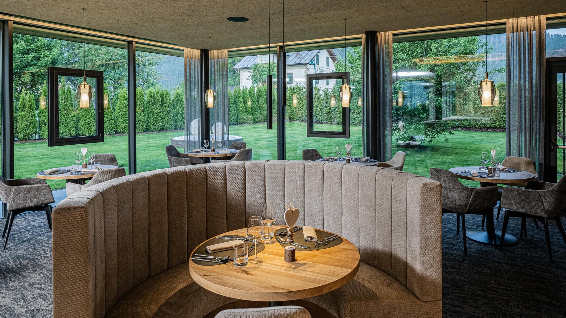 Gemütlicher Essbereich mit runden Tischen und Panoramafenstern zum Garten