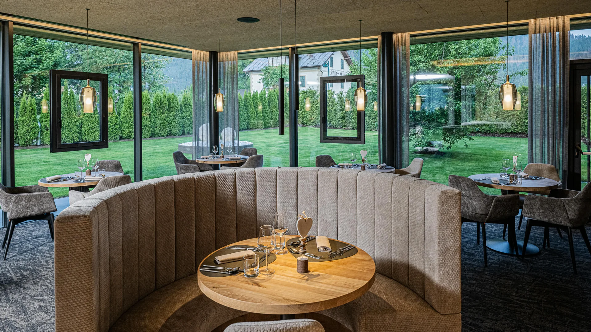 Gemütlicher Essbereich mit runden Tischen und Panoramafenstern zum Garten