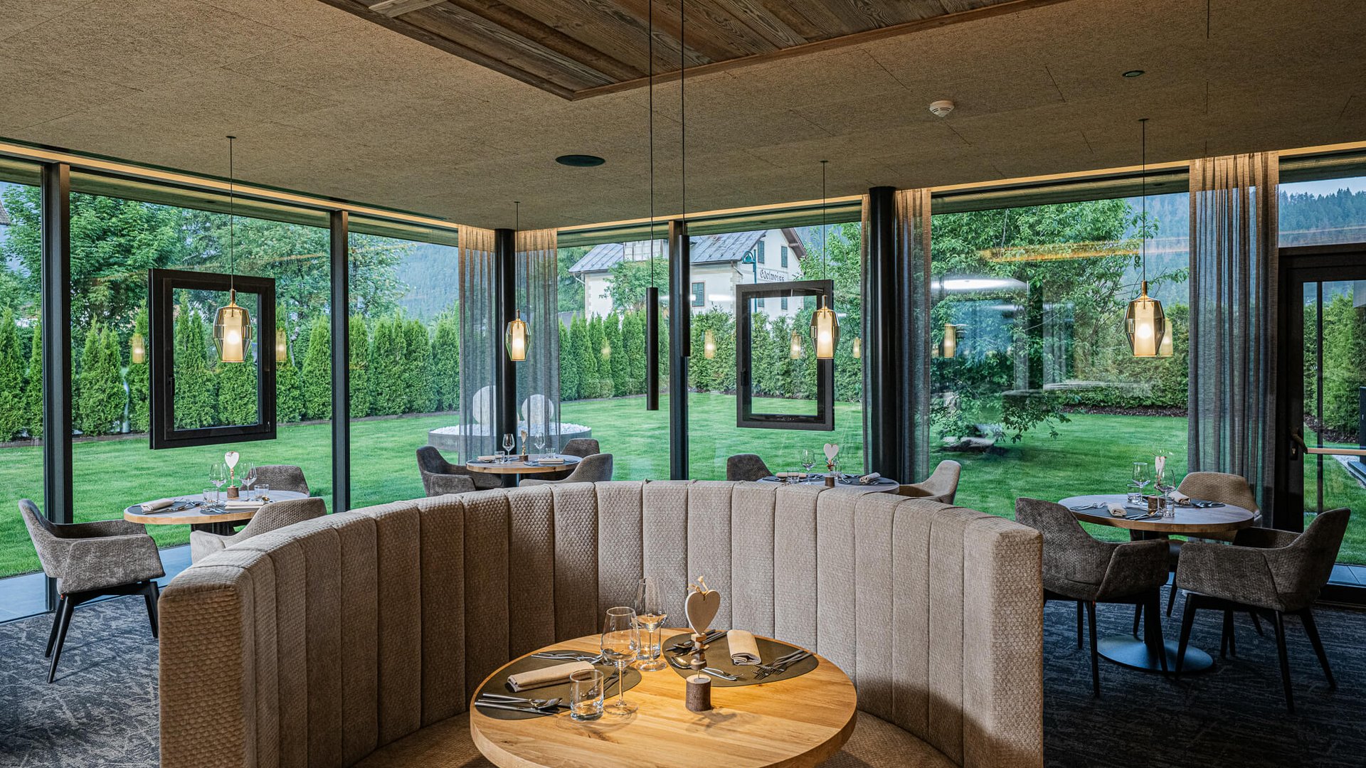 Gemütlicher Essbereich mit runden Tischen und Panoramafenstern zum Garten
