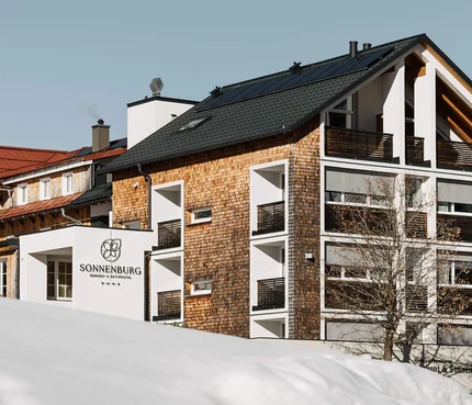 Genuss- und Aktivhotel Sonnenburg © Elisa Moosbrugger Verschneites Hotel Sonnenburg mit Balkonen vor bewaldeter Berglandschaft