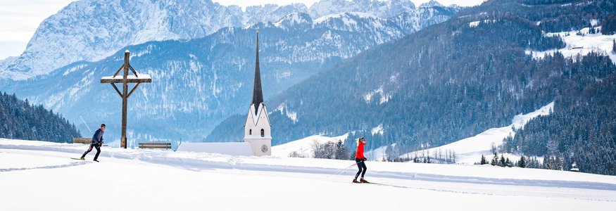 Two cross-country skiers in snowy landscape with church and mountains