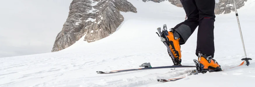 Skibergsteiger steigt mit Steigeisen und Stöcken auf verschneitem Berg auf