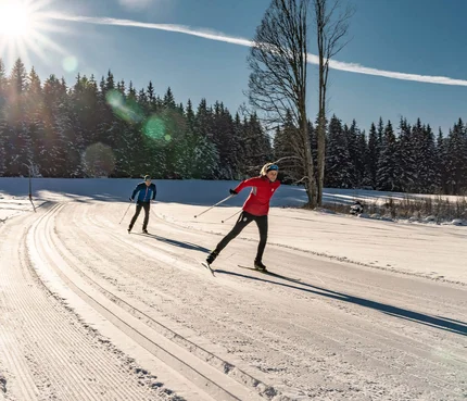 Zwei Personen beim Skilanglauf auf sonniger, verschneiter Strecke