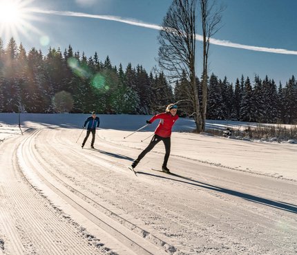 Two people cross-country skiing on a sunny snowy trail