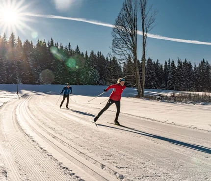 Two people cross-country skiing on a sunny snowy trail