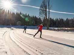 Two people cross-country skiing on a sunny snowy trail