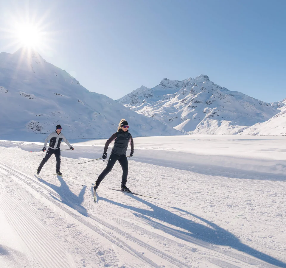 Zwei Personen beim Langlaufen in verschneiter Berglandschaft bei Sonnenschein