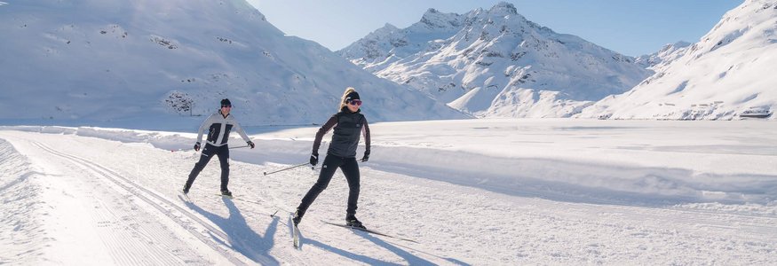 Two people cross-country skiing in snowy mountain landscape with bright sun