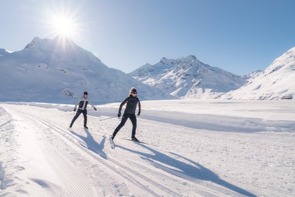 Zwei Personen beim Langlaufen in verschneiter Berglandschaft bei Sonnenschein