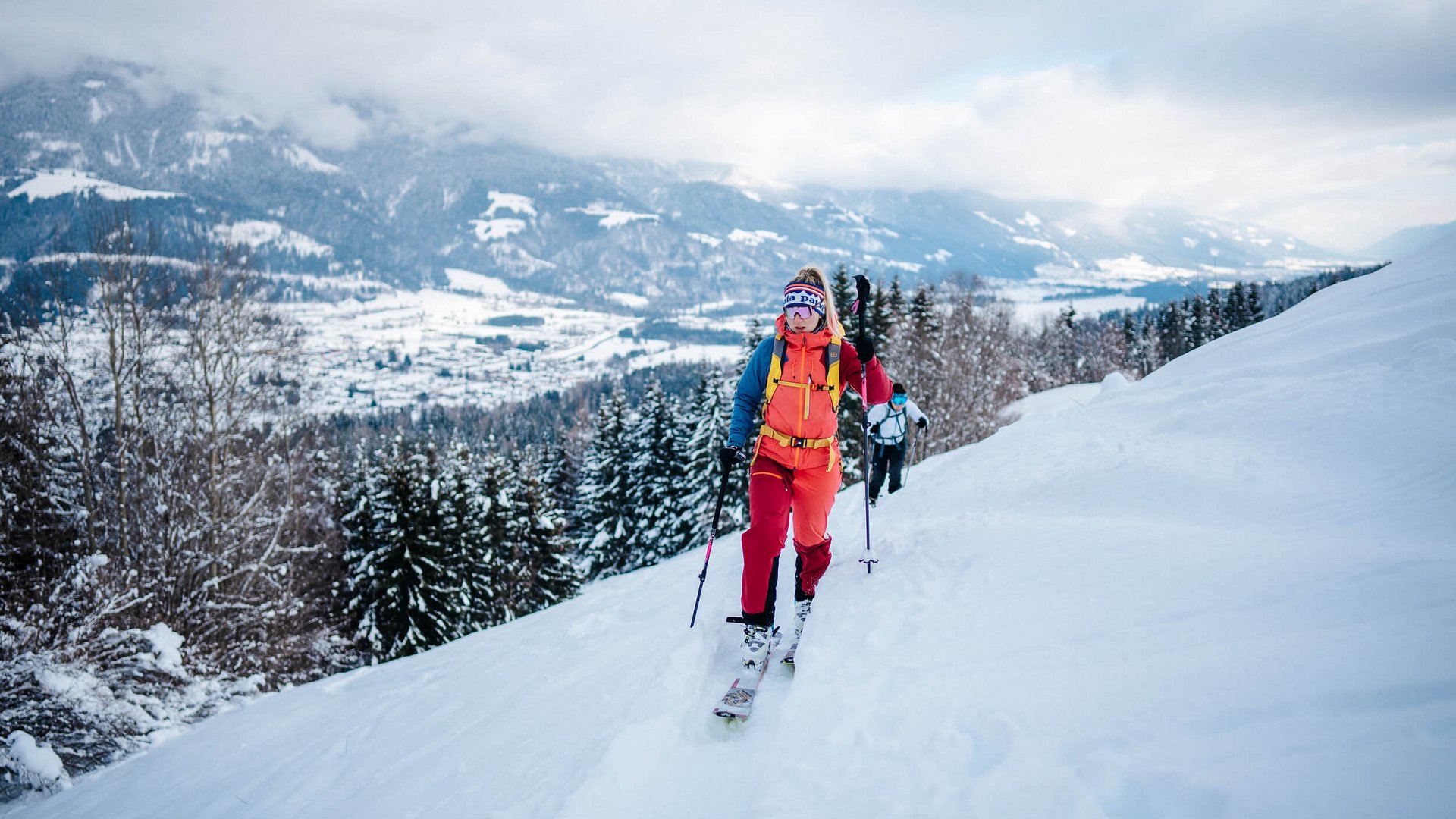 Skier ascending snowy mountain with panoramic valley view in background