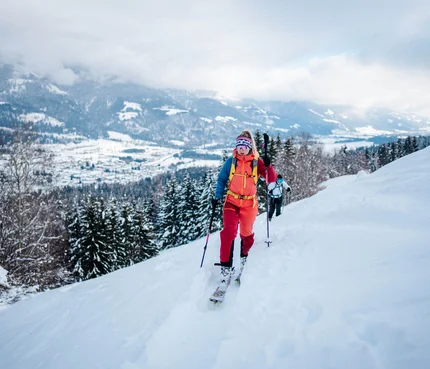 Skifahrerin beim Aufstieg auf verschneitem Berg mit Panorama im Hintergrund