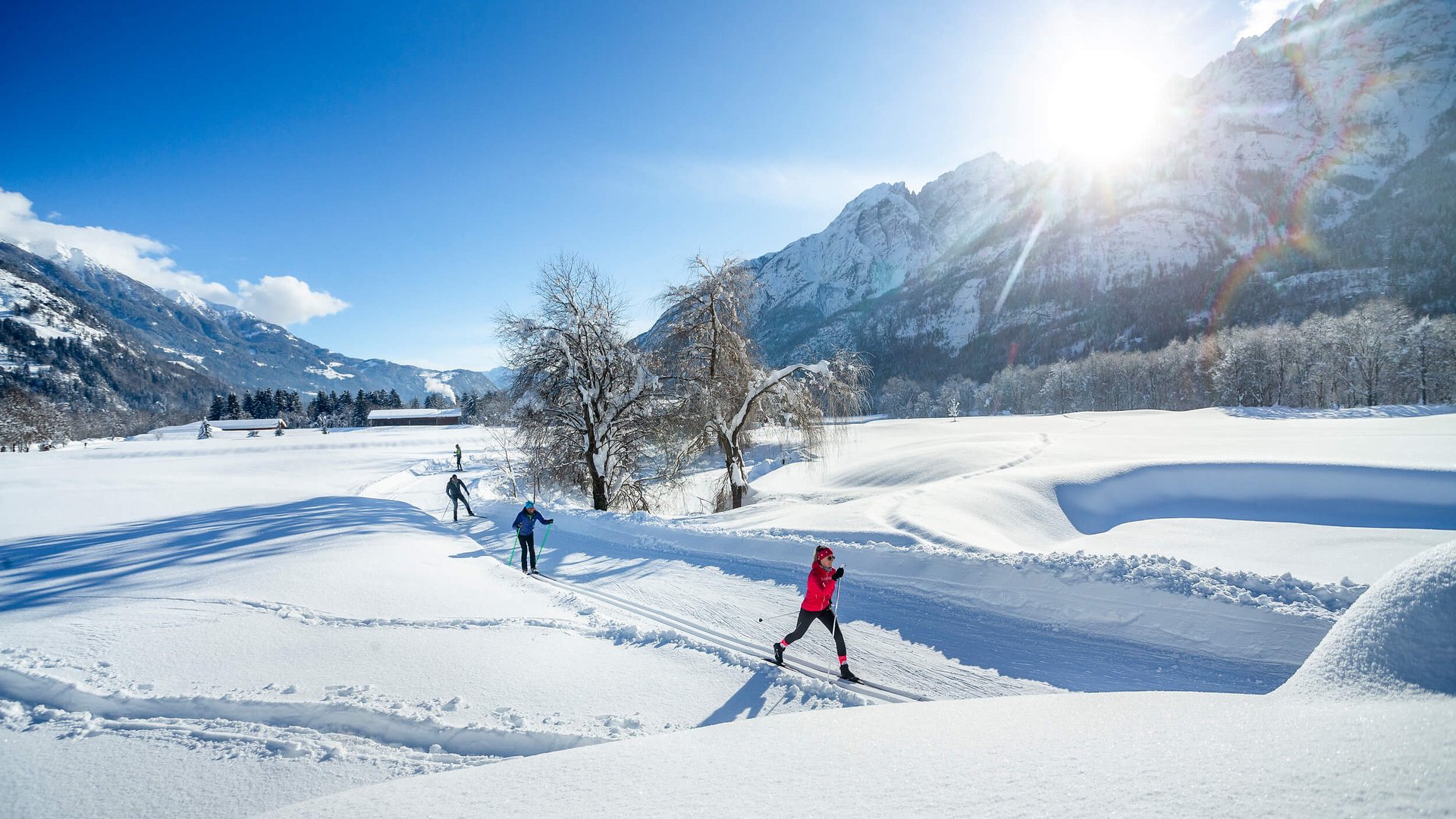 Langläufer im sonnigen, verschneiten Bergtal vor schneebedeckten Bergen