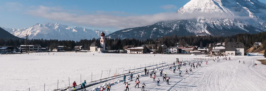 Ganghoferlauf 2025 © Region Seefeld - Sebastian Marko Langläufer beim Rennen vor Bergkulisse mit Kirche im verschneiten Tal