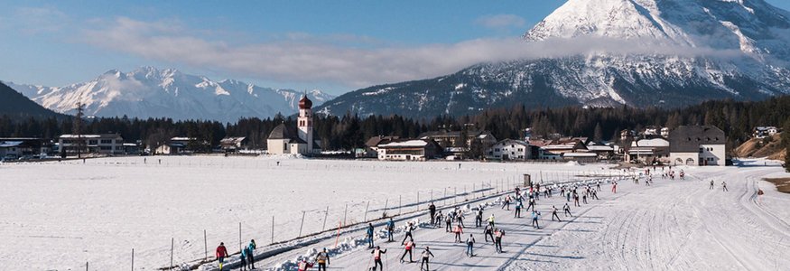 Langläufer beim Rennen vor Bergkulisse mit Kirche im verschneiten Tal