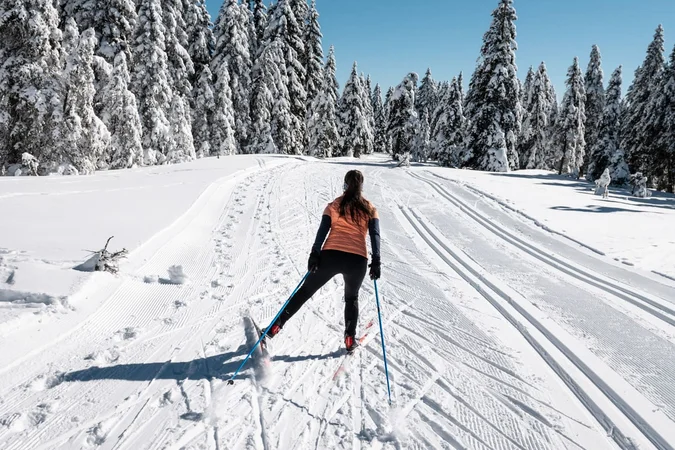 Frau beim Skilanglauf auf verschneiter Winterlandschaft mit Tannenbäumen