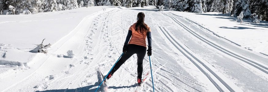 Frau beim Skilanglauf auf verschneiter Winterlandschaft mit Tannenbäumen