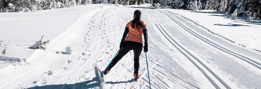 Frau beim Skilanglauf auf verschneiter Winterlandschaft mit Tannenbäumen