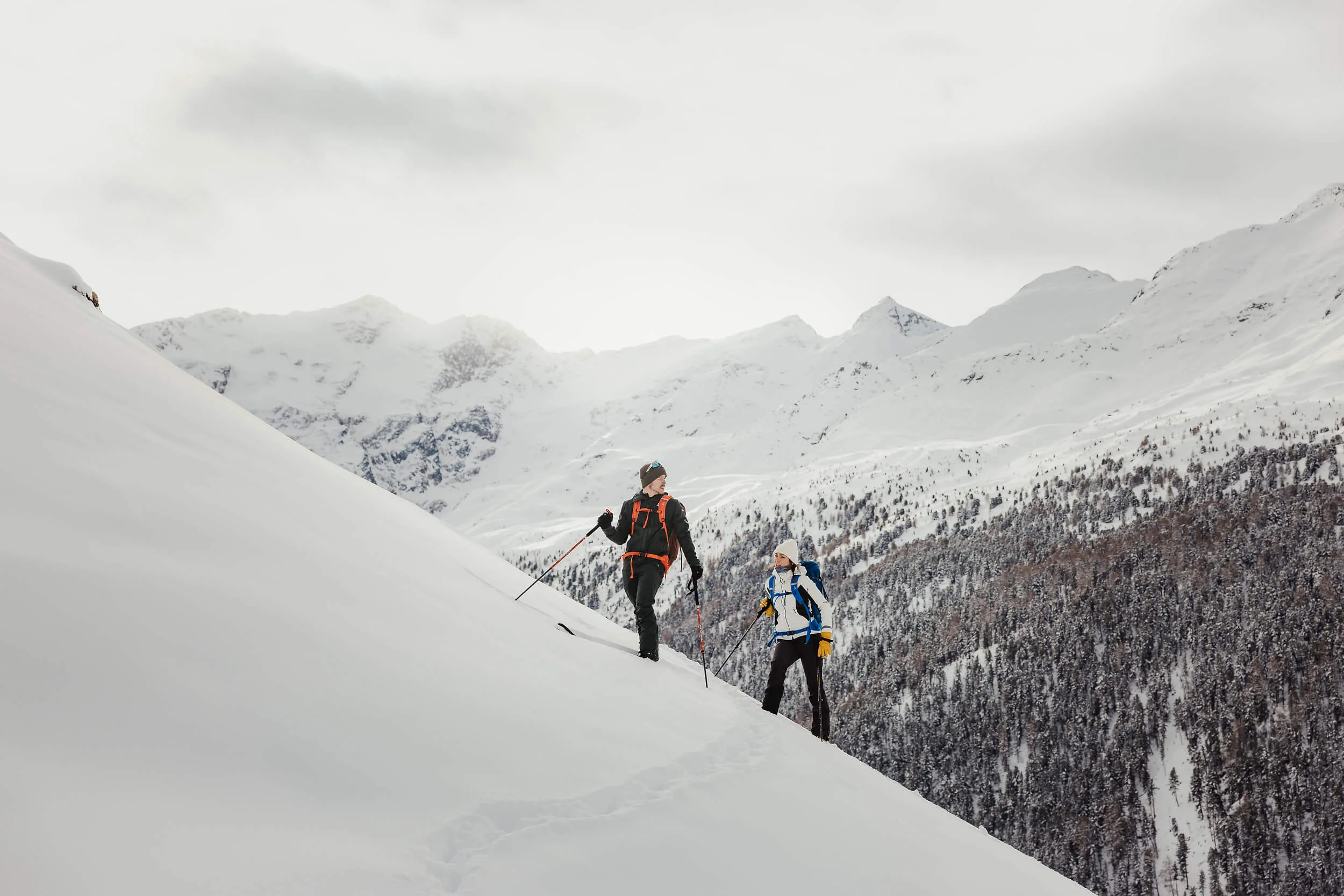 Zwei Wanderer steigen im Schnee an einem steilen Hang in verschneiter Berglandschaft auf