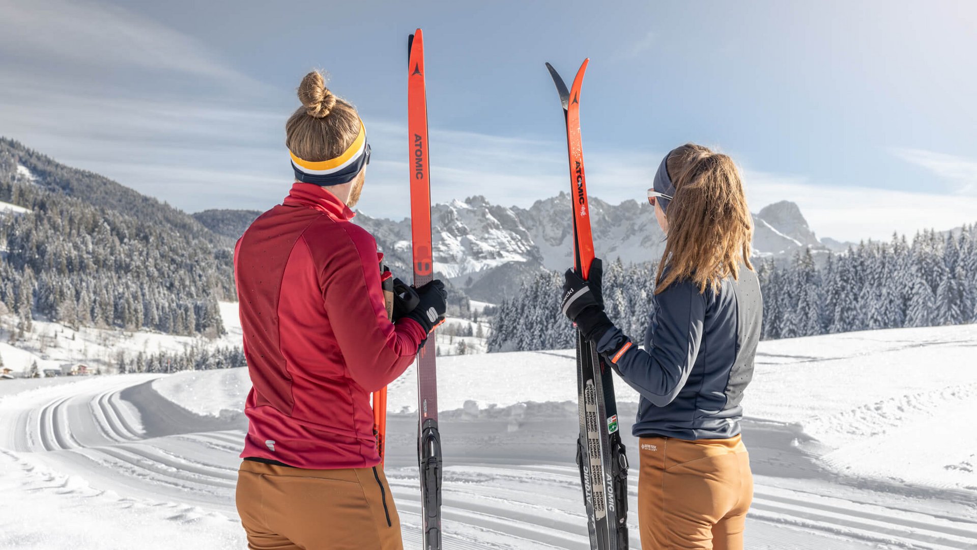 Langlauf Urlaub im Tennengau © Dachstein West Zwei Skifahrer mit roten Skiern blicken auf verschneite Berge bei Sonnenschein