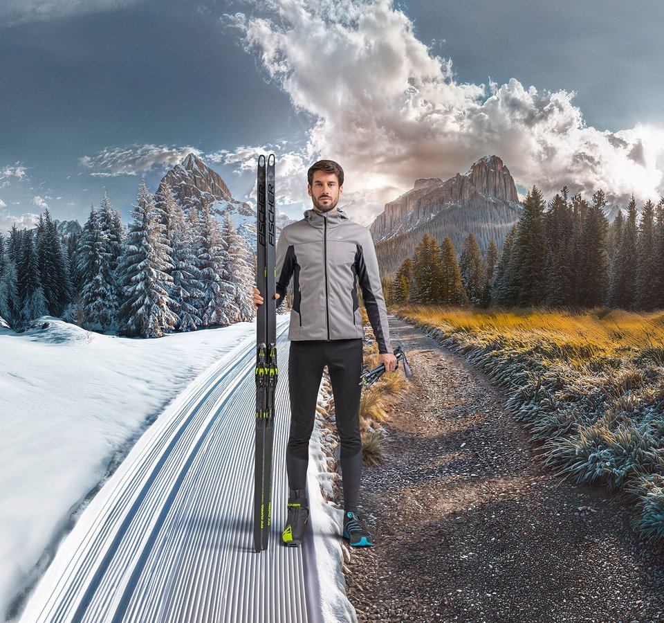 Mann steht an der Grenze zwischen Schnee und Herbst mit Langlaufski