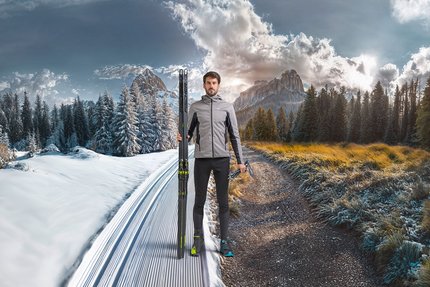 Mann steht an der Grenze zwischen Schnee und Herbst mit Langlaufski