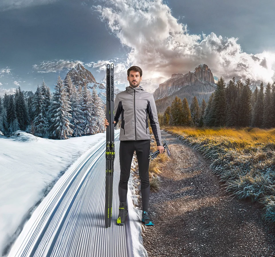 Mann steht an der Grenze zwischen Schnee und Herbst mit Langlaufski