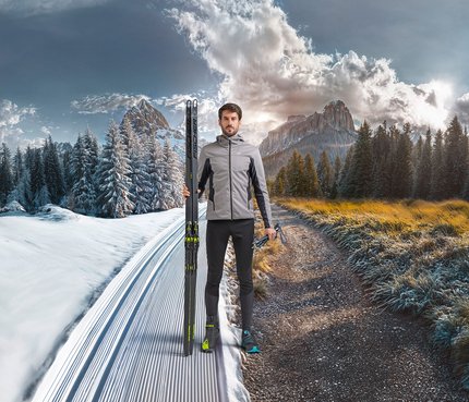 Mann steht an der Grenze zwischen Schnee und Herbst mit Langlaufski
