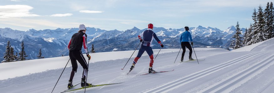 Three cross-country skiers on snowy mountain trail with alpine background