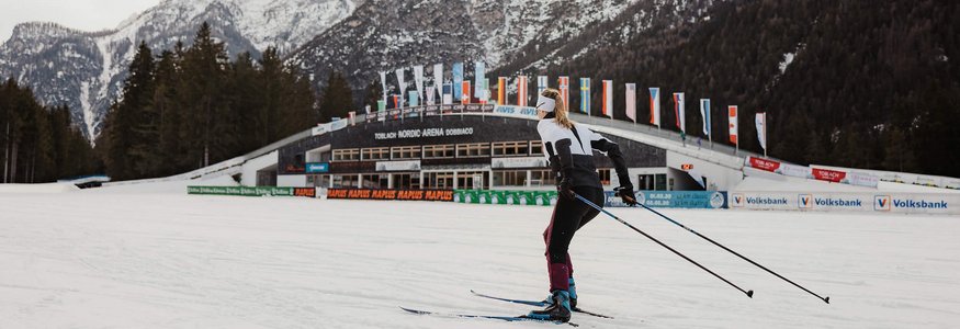 Skilangläufer vor verschneiten Bergen und Nordic Arena in Toblach