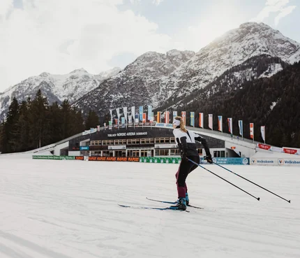 Skilangläufer vor verschneiten Bergen und Nordic Arena in Toblach