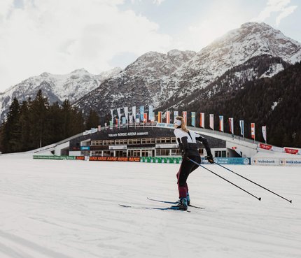 Cross-country skier near snow-covered mountains and Nordic Arena Toblach