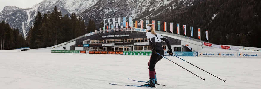 Trainieren wie die Profis in den Drei Zinnen © Alex Moling Skilangläufer vor verschneiten Bergen und Nordic Arena in Toblach
