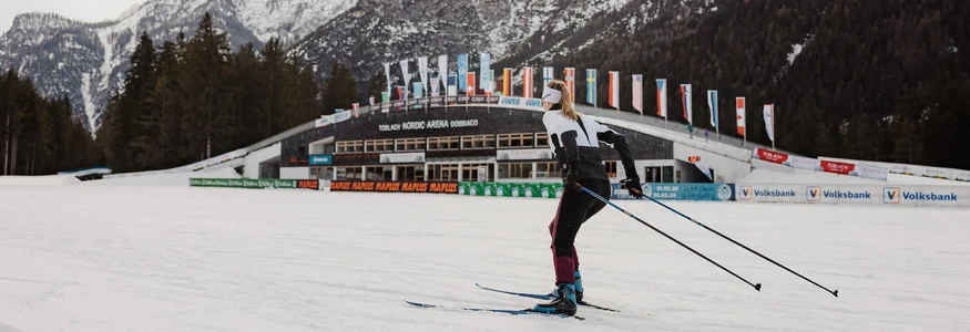 Hotel Union ***S © Alex Moling Skilangläufer vor verschneiten Bergen und Nordic Arena in Toblach