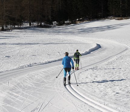Zwei Langläufer auf verschneiter Loipe im Wald